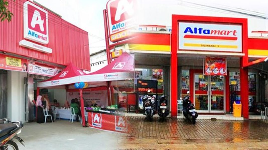 Tampilan depan gerai Alfamart dengan papan nama merah kuning yang ikonik dan deretan parkir motor pelanggan.